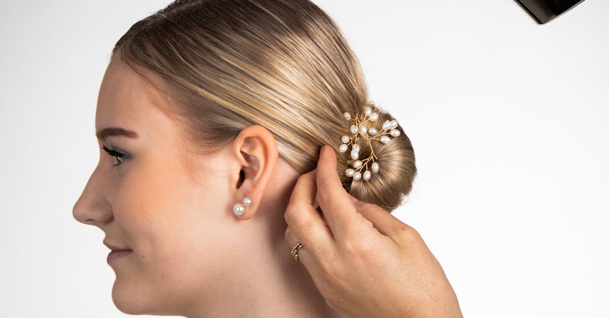 Professional hairstylist applying product to elegant bun on woman with pearl accessory.